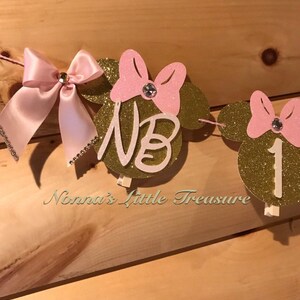May include: Gold glitter Minnie Mouse themed banner with pink bows and rhinestones. The banner says "NB 1".