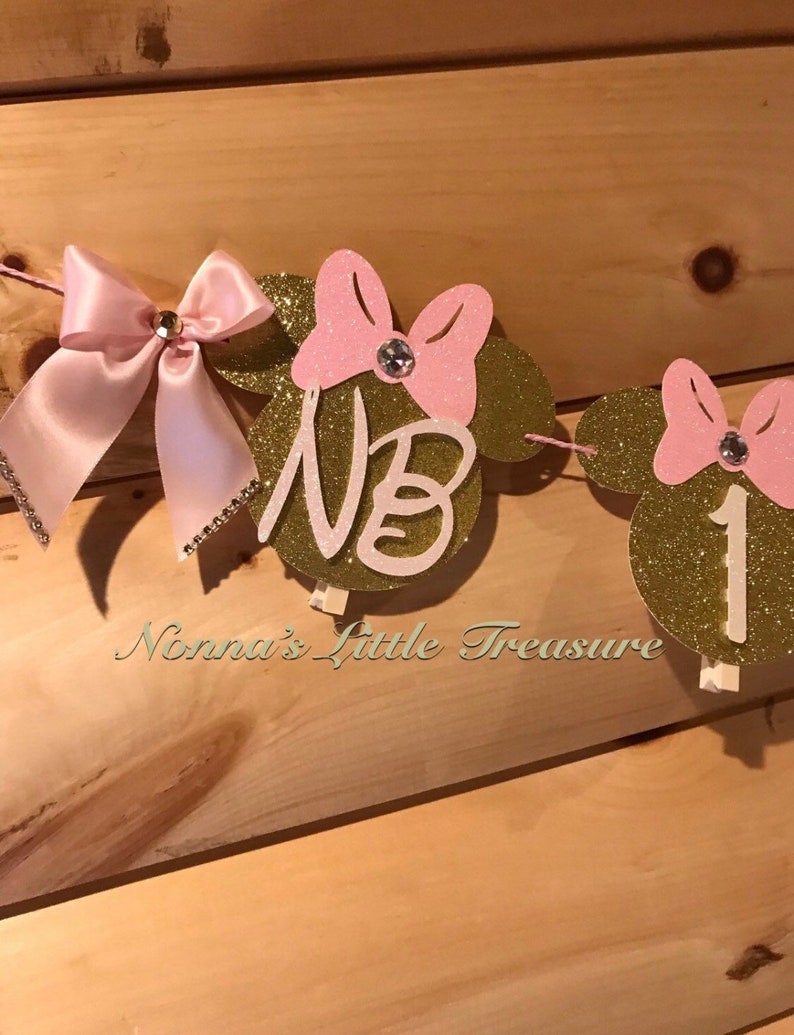 May include: Gold glitter Minnie Mouse themed banner with pink bows and rhinestones. The banner says "NB 1".
