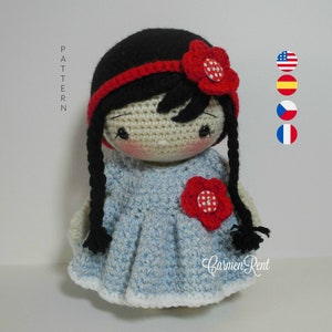 Puede incluir: Muñeca de crochet con cabello negro, una diadema roja y un vestido azul con una flor roja. La muñeca lleva una flor roja con lunares blancos en la cabeza.