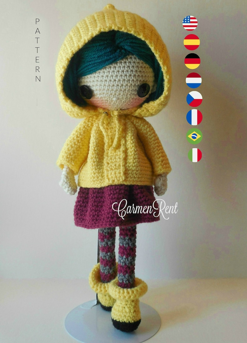 May include: Crocheted doll wearing a yellow raincoat, a burgundy skirt, and striped tights. The doll has green hair and brown eyes. The doll is standing on a white stand. The text "Carmen Rent" is visible on the doll's skirt.