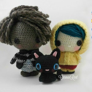 May include: Two crocheted dolls, one with brown hair and a striped sweater, the other with blue hair and a yellow raincoat, stand next to a black crocheted cat.