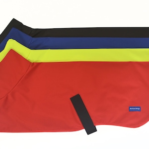 May include: A selection of dog coats in red, yellow, blue, and black. Each coat features a simple design with a collar and a black strap. The coats are made from a smooth, solid-coloured material.