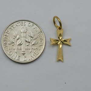 May include: A small gold cross pendant with a diamond-shaped design. The pendant is shown next to a US dime for size comparison.