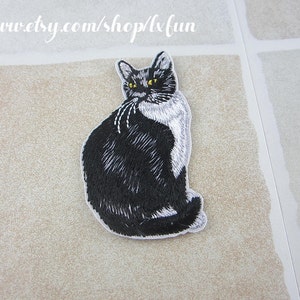 May include: Embroidered patch of a black and white cat with yellow eyes, sitting and looking over its shoulder. The patch has a white border and is on a beige surface. Text at the top reads: www.etsy.com/shop/lxfun.