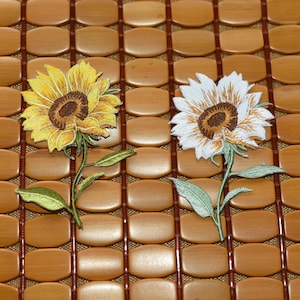 May include: Two embroidered sunflower patches, one with yellow petals and one with white petals, both featuring a dark brown centre and a green stem with two leaves, showcasing detailed stitching and vibrant thread colours for fabric application.