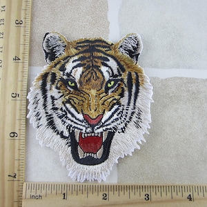 May include: Embroidered tiger patch with a detailed design. The tiger has a fierce expression with its mouth open, revealing teeth and a red interior. The patch is approximately 4 inches wide.