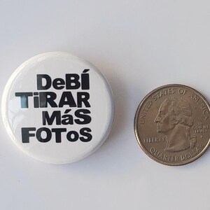 K&ouml;nnte beinhalten: Ein wei&szlig;er Knopf mit dem Text "Deb&iacute; Tirar M&aacute;s Fotos" in Schwarz, neben einer US-Viertel-Dollar-M&uuml;nze. Der Knopf ist rund und gl&auml;nzend. Die M&uuml;nze zeigt ein Profil von George Washington.
