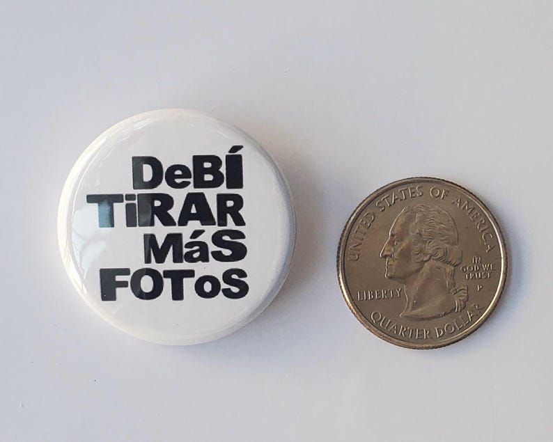 K&ouml;nnte beinhalten: Ein wei&szlig;er Knopf mit dem Text "Deb&iacute; Tirar M&aacute;s Fotos" in Schwarz, neben einer US-Viertel-Dollar-M&uuml;nze. Der Knopf ist rund und gl&auml;nzend. Die M&uuml;nze zeigt ein Profil von George Washington.