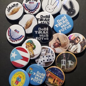 K&ouml;nnte beinhalten: Eine Sammlung runder Ansteckbuttons mit verschiedenen Designs. Einige Buttons zeigen spanischen Text, w&auml;hrend andere Bilder eines Kaninchens, eines Frosches, einer puerto-ricanischen Flagge und anderer Grafiken zeigen. Die Buttons sind in verschiedenen Farben.