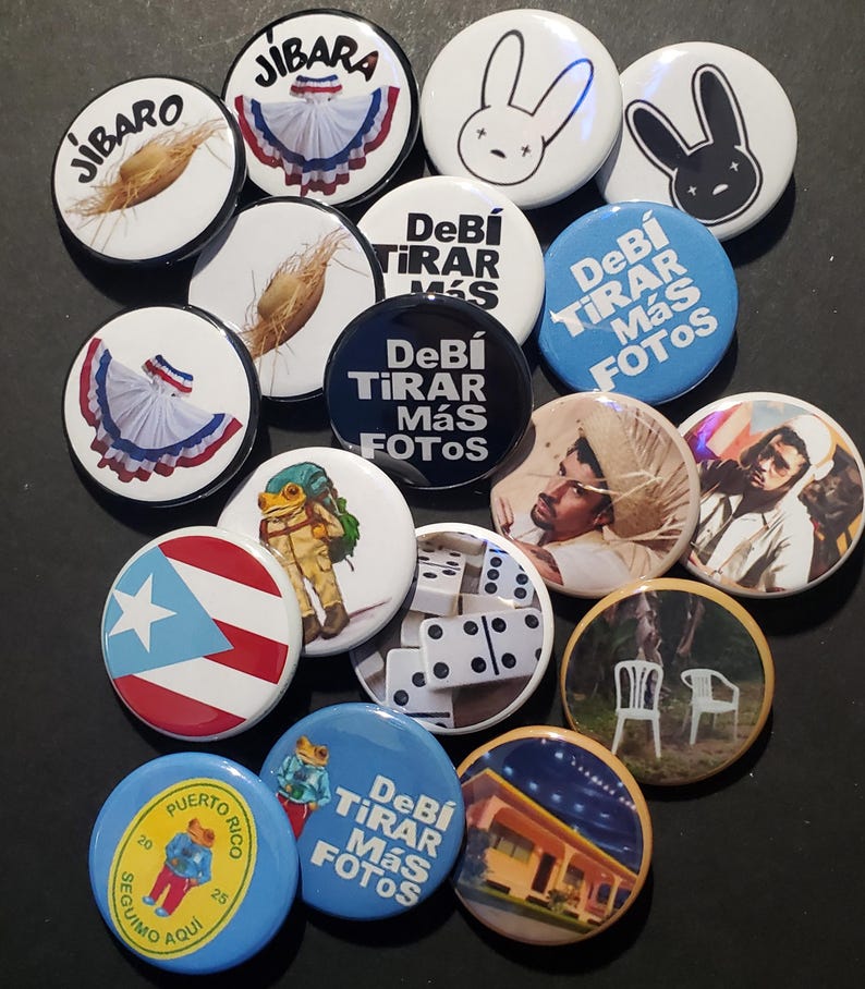 K&ouml;nnte beinhalten: Eine Sammlung runder Ansteckbuttons mit verschiedenen Designs. Einige Buttons zeigen spanischen Text, w&auml;hrend andere Bilder eines Kaninchens, eines Frosches, einer puerto-ricanischen Flagge und anderer Grafiken zeigen. Die Buttons sind in verschiedenen Farben.