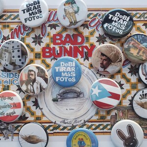 K&ouml;nnte beinhalten: Eine Sammlung bunter runder Buttons mit verschiedenen Designs und Texten, darunter die Worte "BAD BUNNY" und "Puerto Rico". Die Buttons zeigen Bilder, Flaggen und spanische S&auml;tze. Der Hintergrund ist ein dekoratives Fliesenmuster.