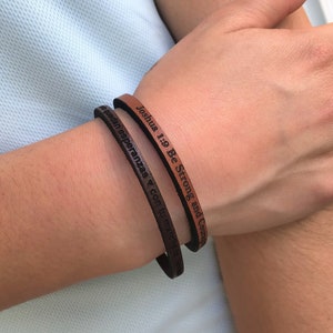 May include: Two leather bracelets with engraved text. One bracelet reads "Joshua 1:9 Be Strong and Courageous" and the other reads "Que queden esperanzas y con tu marcha te lleve".