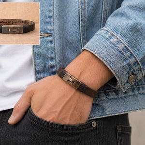 May include: A brown leather bracelet with a rectangular, bronze-colored clasp is shown on a wrist. The bracelet is worn with a denim jacket and a white shirt. The inset image shows the bracelet with the text "...here waiting for you Always..."