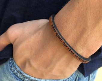 May include: A brown leather bracelet with the text "miles apart, but close to the heart" engraved on it.