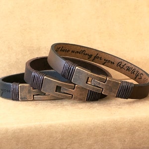 May include: Three leather bracelets in varying shades of brown and black, featuring a metal clasp and decorative stitching. One bracelet has the inscription "here waiting for you always". The bracelets are a stylish accessory.