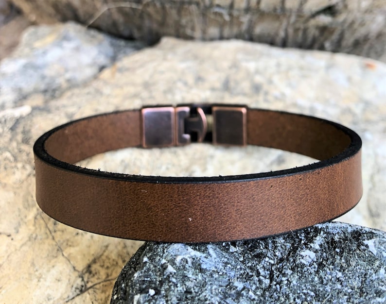 K&ouml;nnte beinhalten: Ein braunes Lederarmband mit einem kupferfarbenen Metallverschluss. Das Armband ist schlicht und elegant und eignet sich hervorragend als Geschenk f&uuml;r jeden Anlass.