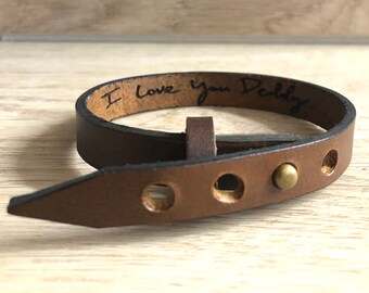May include: Brown leather bracelet with a buckle closure and a metal stud. The bracelet is engraved with the words "I love you Daddy".