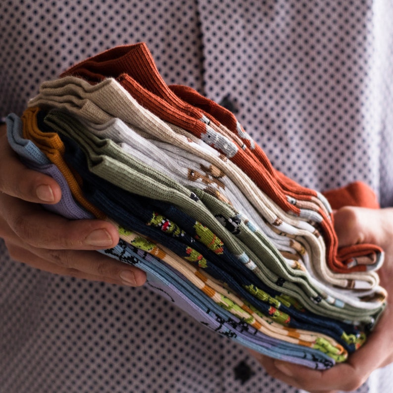 Peut inclure: Une pile de chaussettes color&eacute;es avec diff&eacute;rents motifs, notamment des animaux, des formes g&eacute;om&eacute;triques et des rayures. Les chaussettes sont pli&eacute;es soigneusement et dispos&eacute;es en pile.