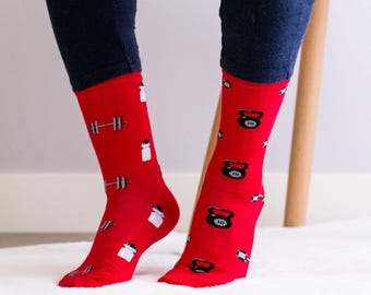 Könnte beinhalten: Ein Paar rote Socken mit einem Muster aus Hanteln, Kettlebells und Wasserflaschen. Die Socken werden von einer Person getragen.