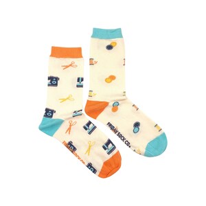 May include: A pair of white socks with a colorful pattern of sewing machines, scissors, spools of thread, and buttons. The socks have orange and blue trim. The text "FRIDAY SOCK CO." is printed on the socks.