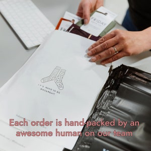 Peut inclure: Une enveloppe blanche avec une illustration en noir et blanc de deux chaussettes. Le texte "It's good to be different." est imprim&eacute; sous les chaussettes. L'enveloppe est plac&eacute;e dans un sac d'exp&eacute;dition en plastique noir. Le texte "Each order is hand-packed by an awesome human on our team" est imprim&eacute; en bas de l'image.
