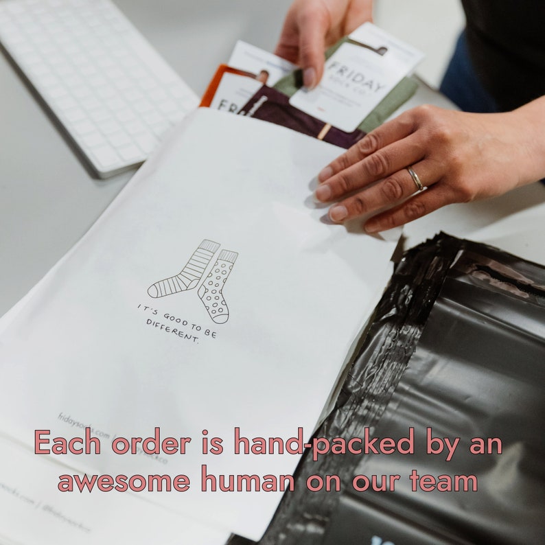 Peut inclure: Une enveloppe blanche avec une illustration en noir et blanc de deux chaussettes. Le texte "It's good to be different." est imprim&eacute; sous les chaussettes. L'enveloppe est plac&eacute;e dans un sac d'exp&eacute;dition en plastique noir. Le texte "Each order is hand-packed by an awesome human on our team" est imprim&eacute; en bas de l'image.