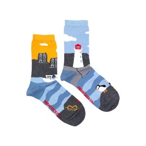 May include: A pair of colourful socks featuring a lighthouse, houses, and a puffin against a blue and grey background. The socks have the text "FRIDAY SOCK CO." on the side.