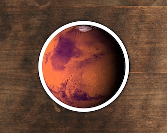 May include: A close-up of a sticker depicting the planet Mars. The sticker is round and has a white border. The surface of Mars is depicted in shades of orange and red, with visible craters and other surface features.