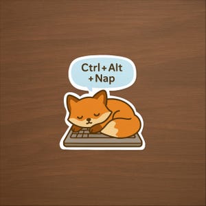 May include: A sticker featuring a cartoon fox napping on a keyboard. The fox is orange and white, with closed eyes. A light blue speech bubble above the fox reads "Ctrl + Alt + Nap". The sticker is on a brown wooden surface.