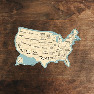 May include: A blue and white map of the United States with each state labeled. The map is on a brown wooden background.