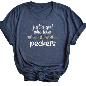 May include: A dark blue t-shirt with the text "just a girl who loves peckers" and a row of colorful cartoon chickens.