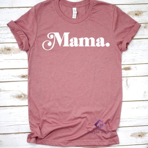 May include: A mauve colored t-shirt with the word "Mama" printed in white on the front. The shirt has a crew neck and short sleeves.