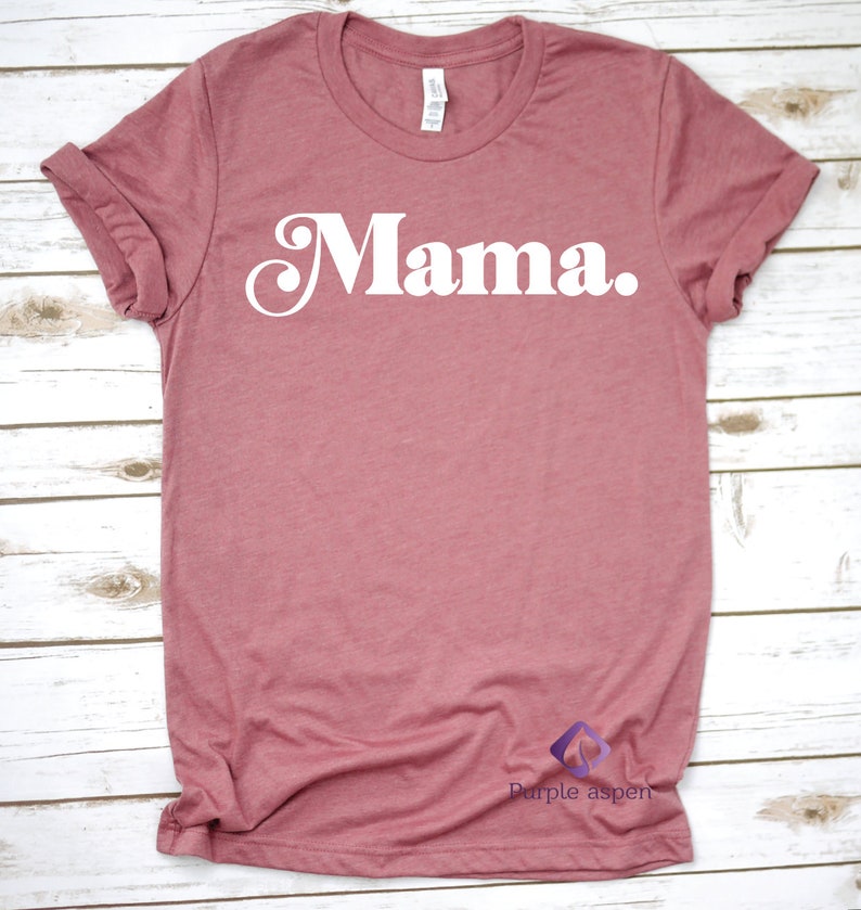 May include: A mauve colored t-shirt with the word "Mama" printed in white on the front. The shirt has a crew neck and short sleeves.