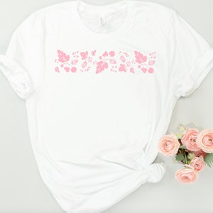 May include: White t-shirt with a pink floral design across the chest.