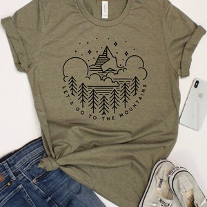 Op de afbeelding: Een groen T-shirt met een zwart grafisch ontwerp van een bergketen, bomen en sterren. De tekst "Let's go to the mountains" staat rond de afbeelding.