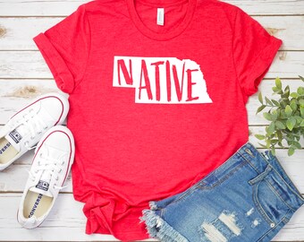 May include: Red t-shirt with a white outline of the state of Nebraska and the word "NATIVE" written in white inside the outline.