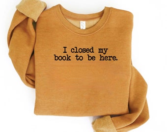 May include: A mustard yellow sweatshirt with the text "I closed my book to be here." printed in black.