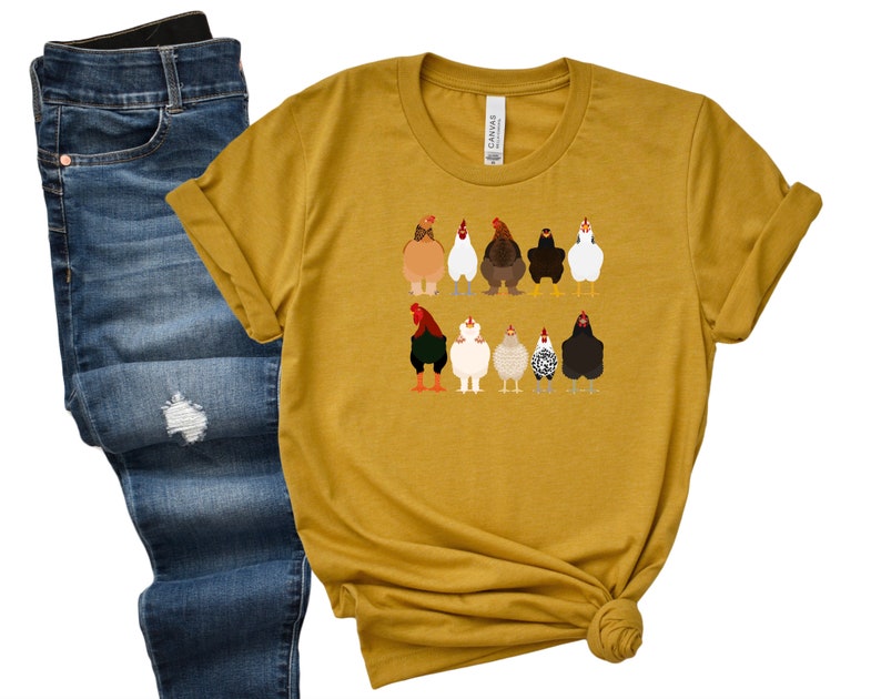May include: A mustard yellow t-shirt featuring a graphic of a line of chickens in various colours and patterns.