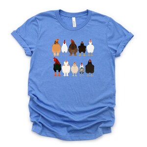 May include: A light blue t-shirt featuring a graphic of nine chickens in various colours and patterns. The chickens are arranged in two rows, with the top row containing five chickens and the bottom row containing four chickens.