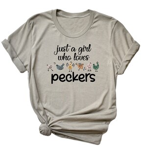 May include: A light gray t-shirt with the text "just a girl who loves peckers" and a row of colorful chickens printed on the front.