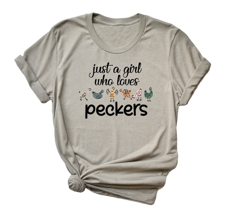 May include: A light gray t-shirt with the text "just a girl who loves peckers" and a row of colorful chickens printed on the front.