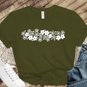 Puede incluir: Una camiseta verde con un diseño floral blanco. El diseño presenta una fila de flores estilizadas con pétalos redondeados.
