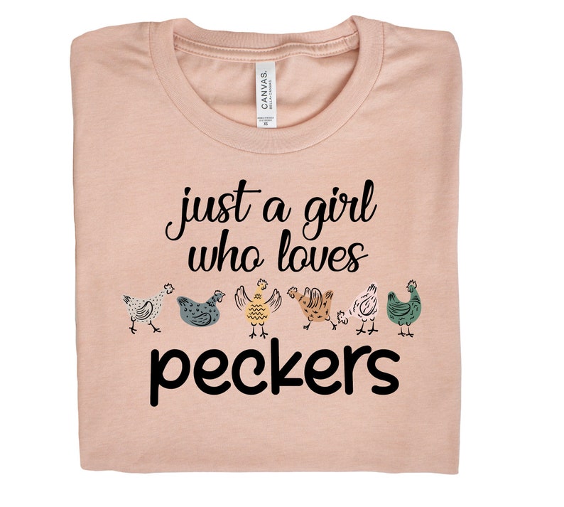 May include: A light pink t-shirt with the text "just a girl who loves peckers" in black. There are six cartoon chickens in a row below the text.