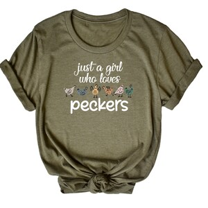 May include: A green t-shirt with the text "Just a girl who loves peckers" and a row of colorful chickens printed on the front.