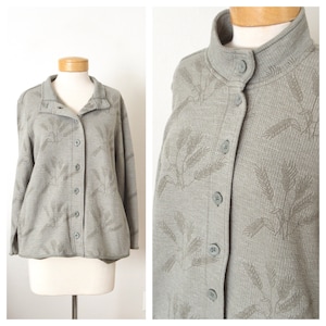 May include: A gray button-up jacket with a long sleeve and a subtle wheat pattern. The jacket has a collar and a button closure.