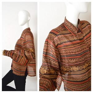 May include: A long-sleeved, sheer button-down shirt with a geometric pattern in shades of brown, orange, and black. The shirt has a relaxed fit and a collar.