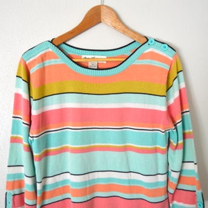 May include: A striped sweater with a light blue, pink, white, and yellow color scheme. The sweater has a boat neck and buttons on the shoulders.