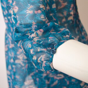 K&ouml;nnte beinhalten: Eine Bluse mit blauem und rosafarbenem Blumendruck und einem Knopfdetail am &Auml;rmel.