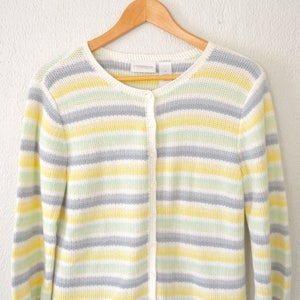 May include: A white, yellow and grey striped cardigan with a button fastening. The cardigan is made from a soft, knitted fabric.