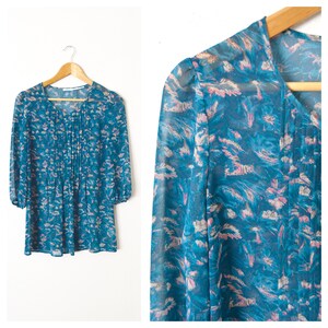 K&ouml;nnte beinhalten: Eine blaue und rosafarbene, florale, durchsichtige Bluse mit V-Ausschnitt und 3/4-&Auml;rmeln.